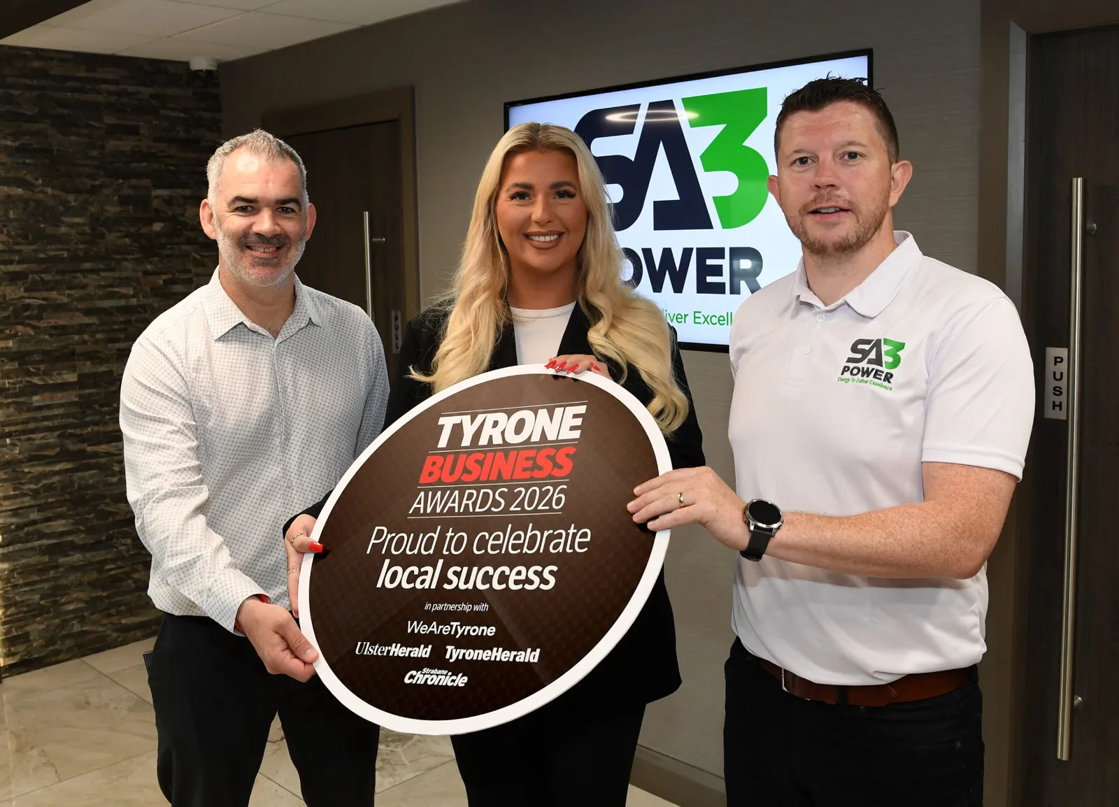 Martin Conway and Holly Cassidy of SA3 POWER with Sean McIntosh of the Tyrone Business Awards holding a Tyrone Business Awards 2026 sign